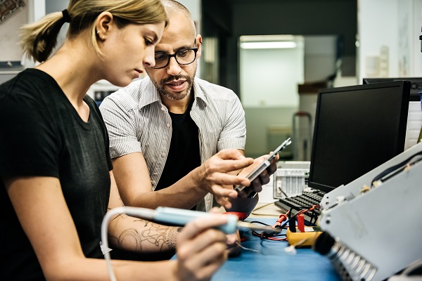 Technician guiding female trainee in workshop.